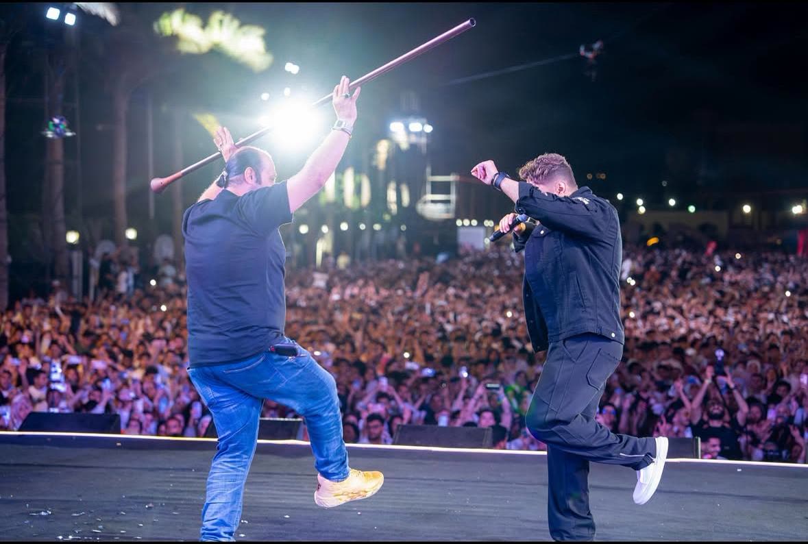Tamer Hosny jumping on stage with a guest